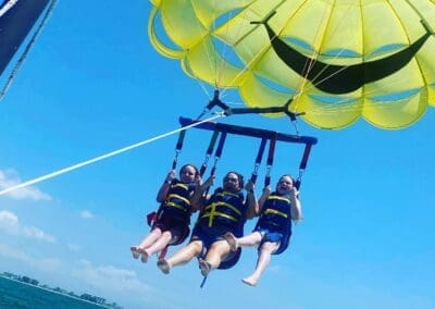Three people parasailing over a clear blue sky, wearing life vests, enjoying an adventurous experience in Clearwater, Florida, highlighting fun vacation activities offered by Orange Grove Travel Company.