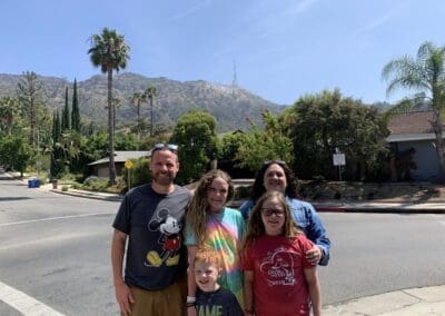 Family posing outdoors with a view of mountains in the background, featuring Disney-themed attire, reflecting personal travel experiences shared by Misty Oerther at Orange Grove Travel Company.