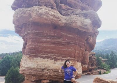Woman posing next to a large rock formation at Garden of the Gods, showcasing natural beauty and outdoor adventure.