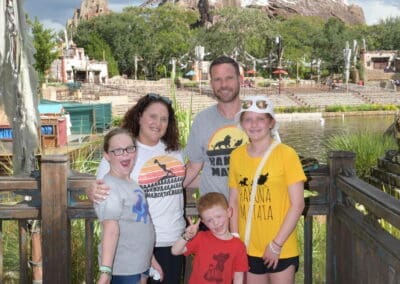 Family posing together in front of a scenic backdrop at a theme park, showcasing joyful expressions and wearing matching vacation attire, emphasizing personal travel experiences related to family trips.