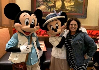 Woman posing with Mickey and Minnie Mouse characters at Disneyland, showcasing a joyful interaction in a themed dining setting.