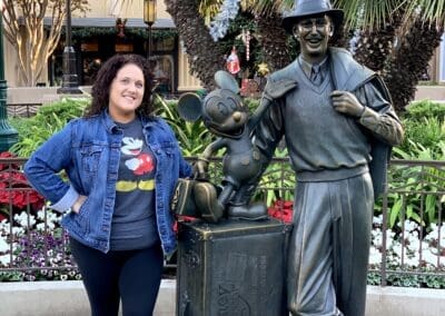 Misty Oerther posing with a bronze statue of Walt Disney and Mickey Mouse at Disneyland, showcasing her personal travel experience and connection to Disney destinations.