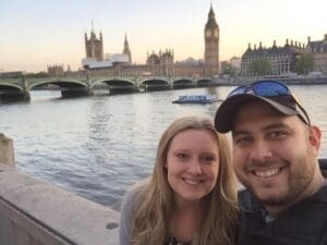 IMG_3336 - Copy Couple smiling for a selfie by the River Thames with the iconic Big Ben and Houses of Parliament in the background, showcasing a memorable travel experience in London.