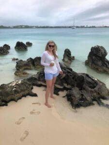 erin-beach Woman in beach attire standing on rocks by the water, showcasing a tropical getaway, reflecting travel planning expertise of Orange Grove Travel Company.